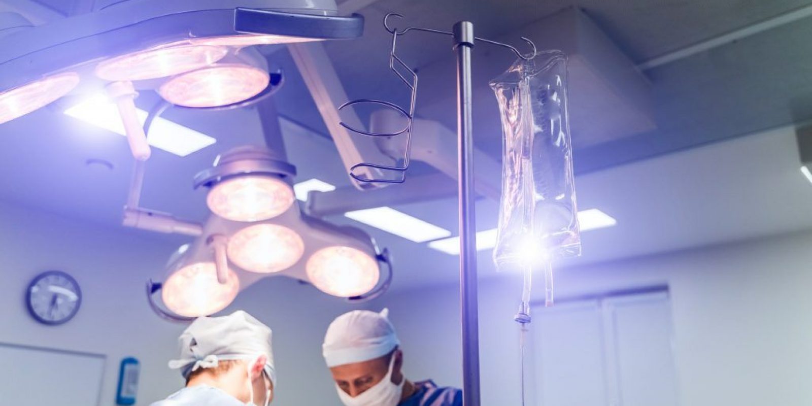 Process of surgery operation using medical equipment. Two surgeons in operating room with surgery equipment and in binocular glasses. Medical background.
