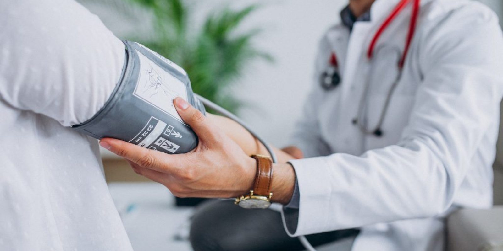 Young male psysician with patient measuring blood pressure