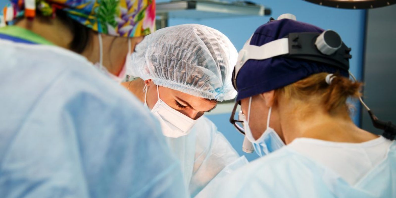 Surgery, medicine and people concept - three surgeons in operating room at hospital during their work.