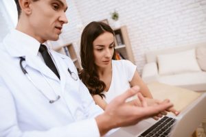 Doctor is showing something on laptop to a pregnant girl.