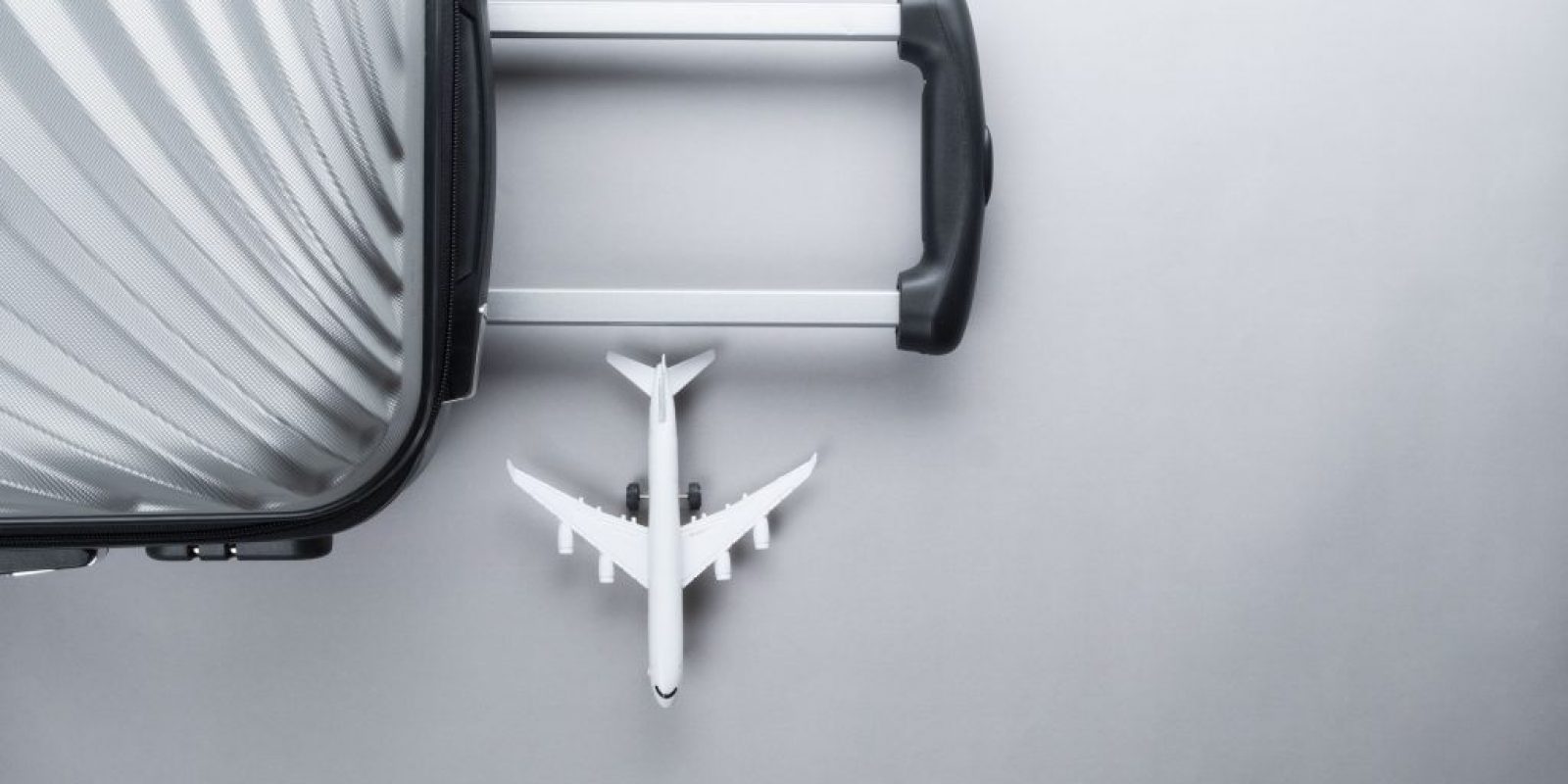 Flat lay grey suitcase with mini airplane on grey background. tr